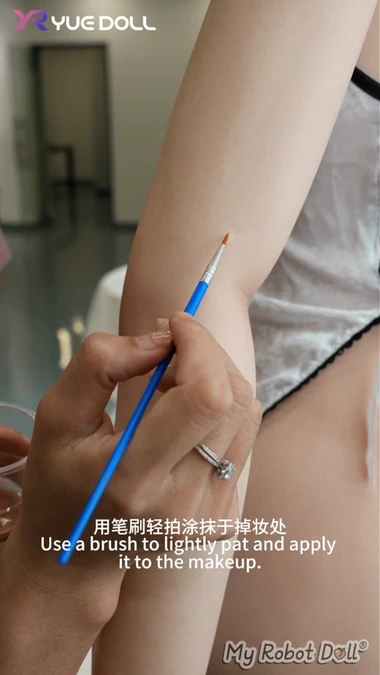 A Fine Brush Applies Makeup To A Small Area On A Yue Doll Arm.